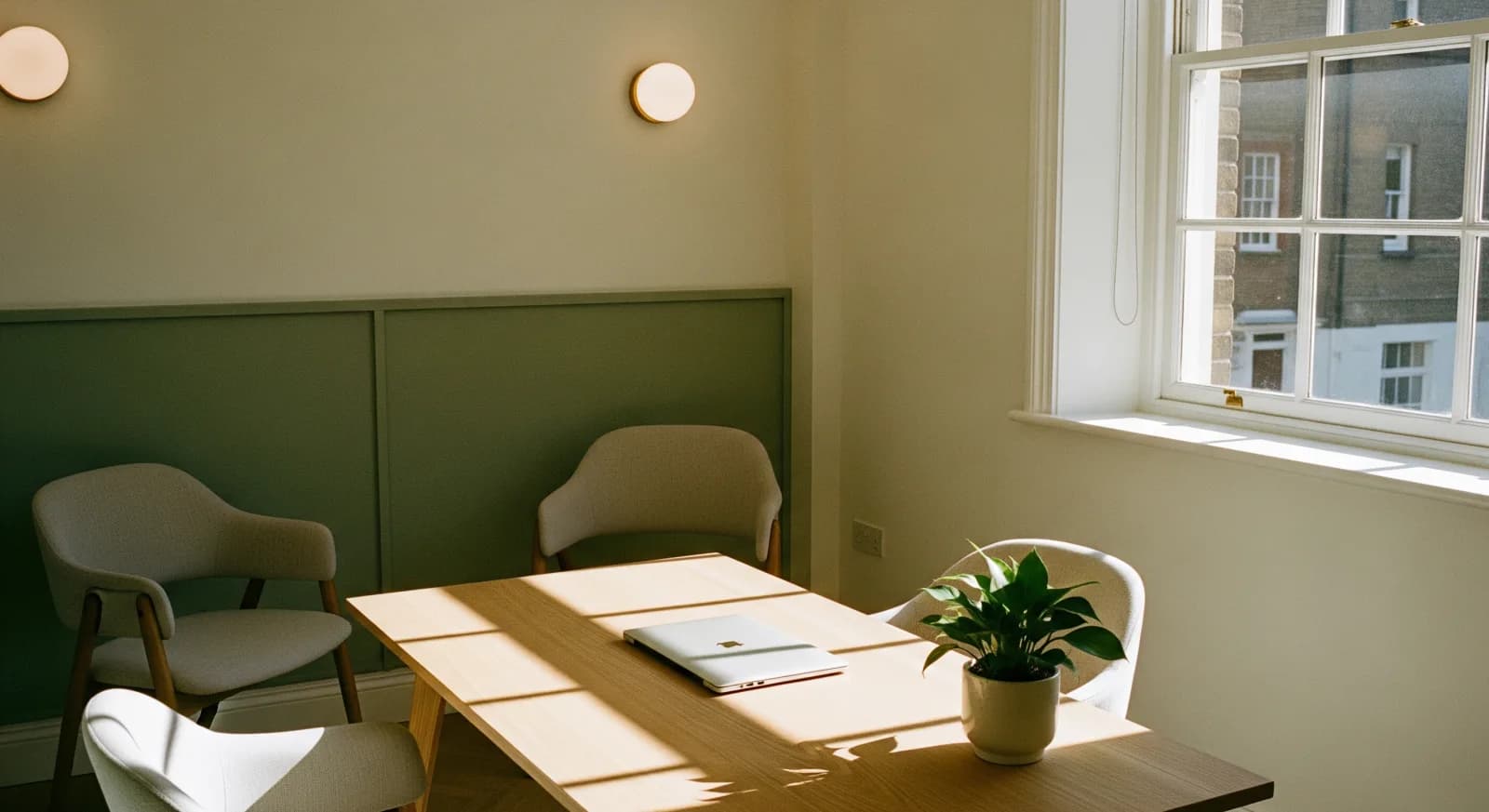 A calm, sunlit clinic consultation room with a wooden table and soft green panelling